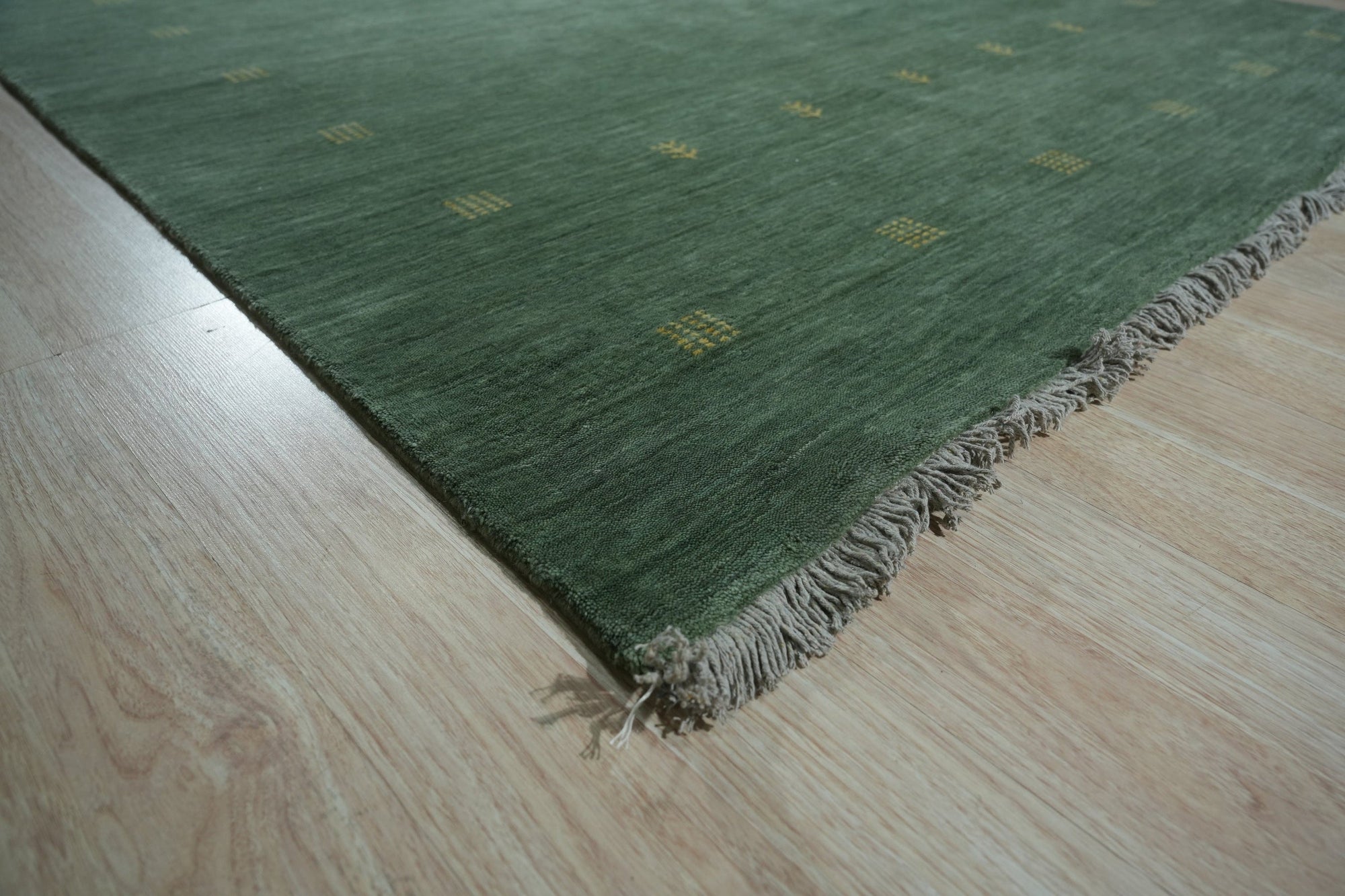 Laine Amara Green Handmade Wool Rug displayed on a light hardwood floor. Lush green tones blend seamlessly in this handcrafted wool rug, its subtle texture adding depth and warmth to the room.