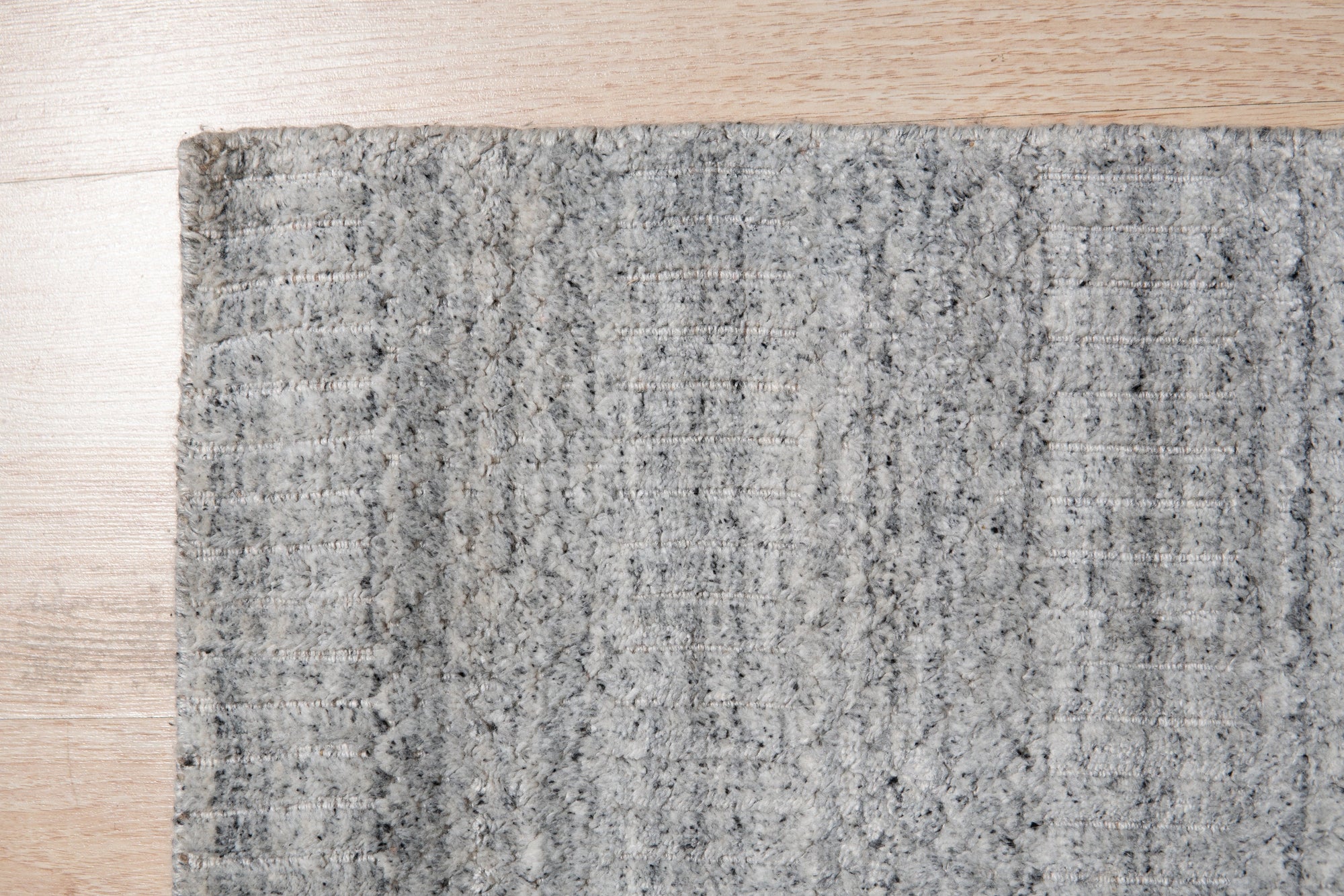 Tessa Xena Silver Handmade Wool Rug, blending cool silvers and neutral tones in a hand-knotted construction, rests in a bright, modern living room setting, lending subtle texture and sophisticated style.