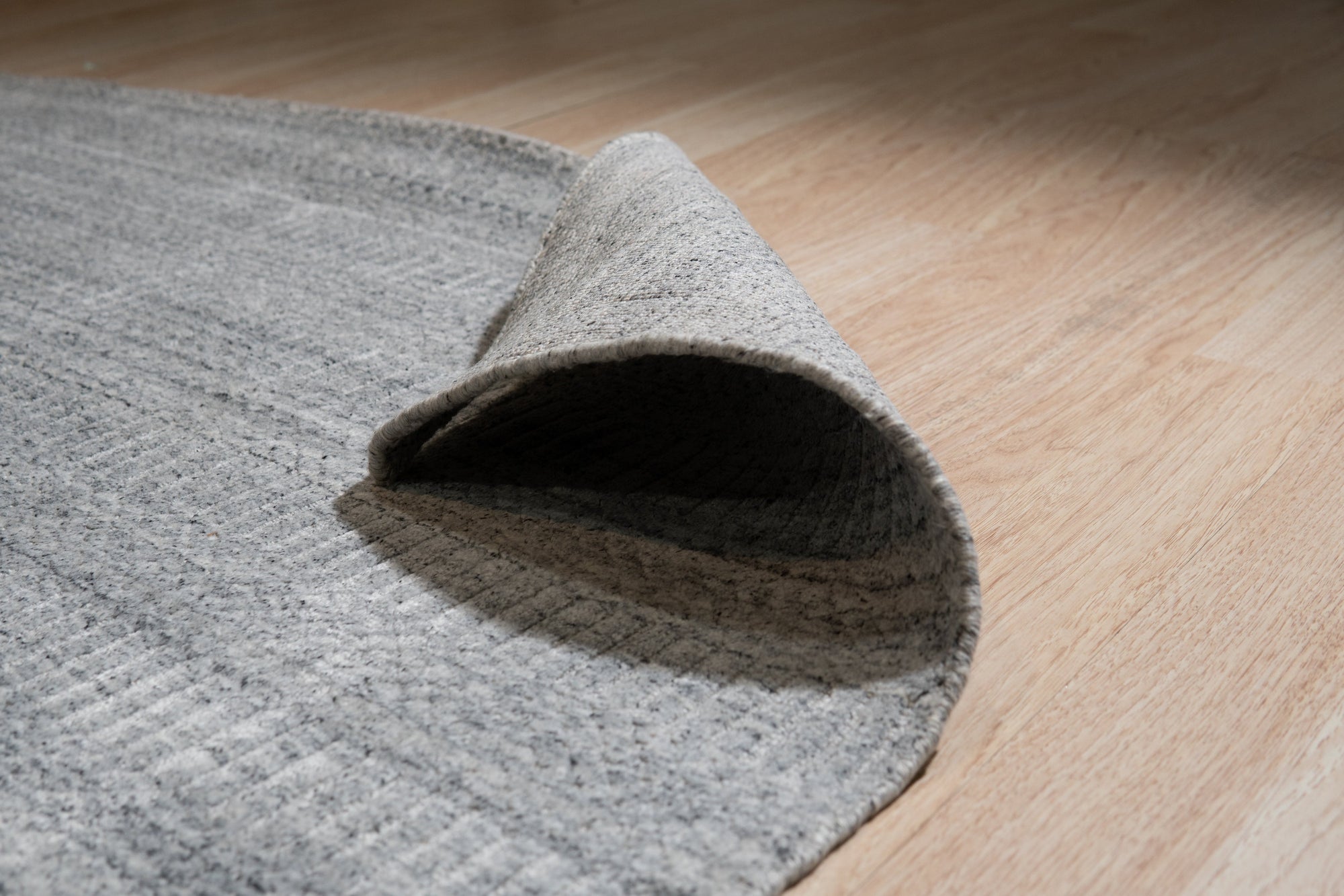 Tessa Xena Silver Handmade Wool Rug, a subtly shimmering silver wool rug with a textured, organic pattern, partially visible in a room setting.