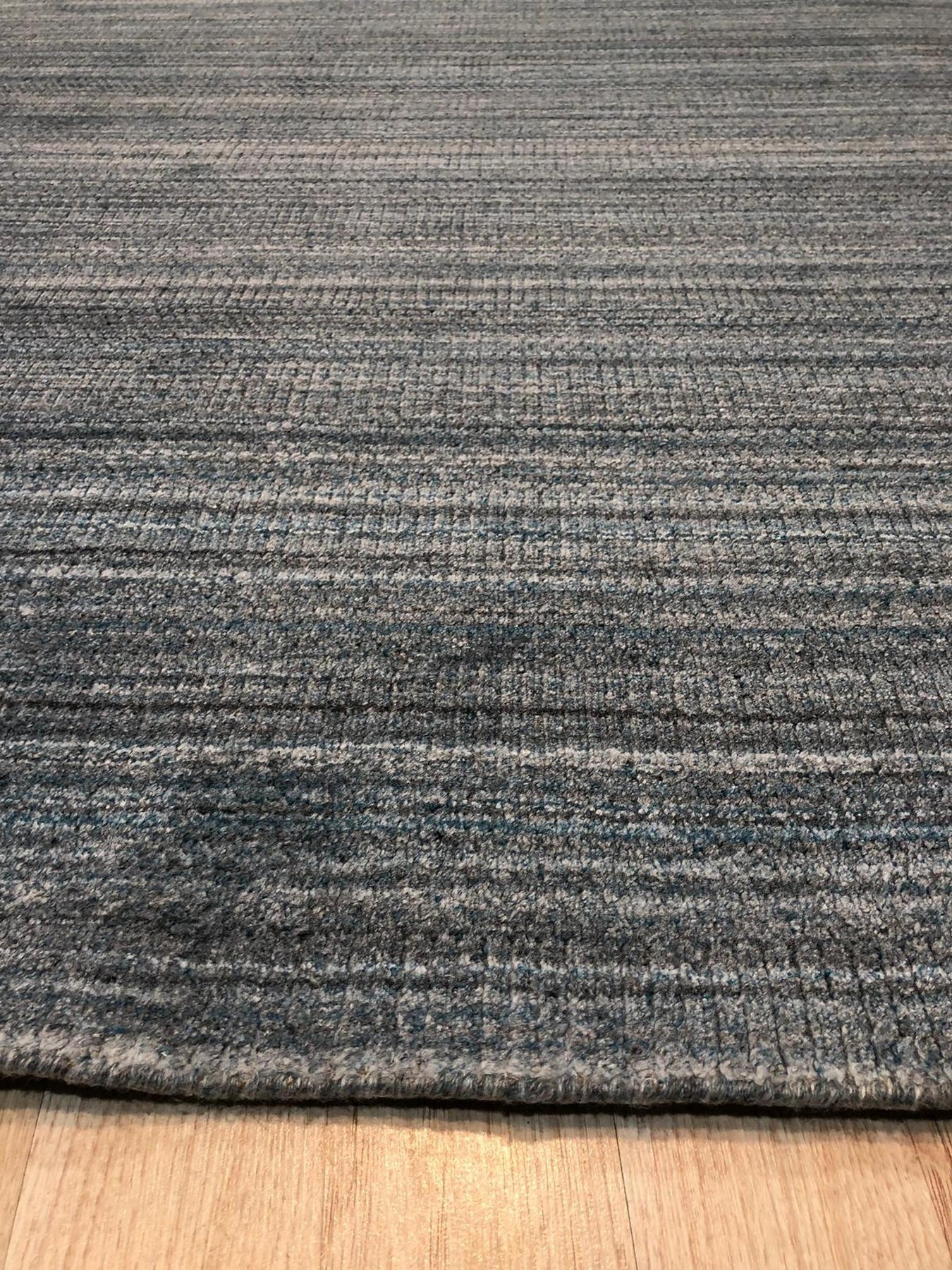 Para Elena Blue Handmade Wool Rug, showcasing intricate geometric patterns in shades of blue, cream, and terracotta. Hand-knotted wool rug displayed on a light hardwood floor, offering a warm and inviting feel. Soft light highlights the rug's textured surface and vibrant color variations.