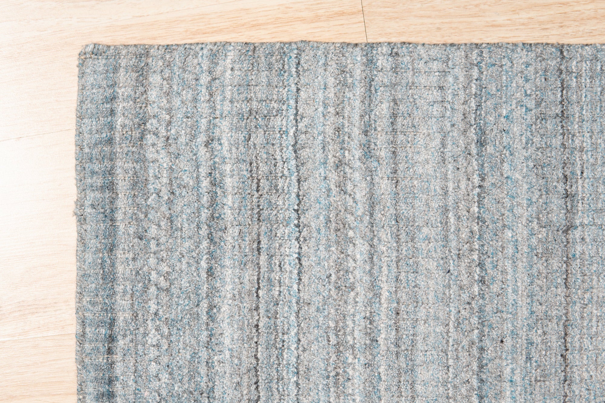 Para Elena Blue Handmade Wool Rug displayed in a warmly lit living space; its intricate, geometric pattern in shades of blue and cream complements the neutral decor and dark wood flooring, highlighting its hand-knotted wool construction and sophisticated design.