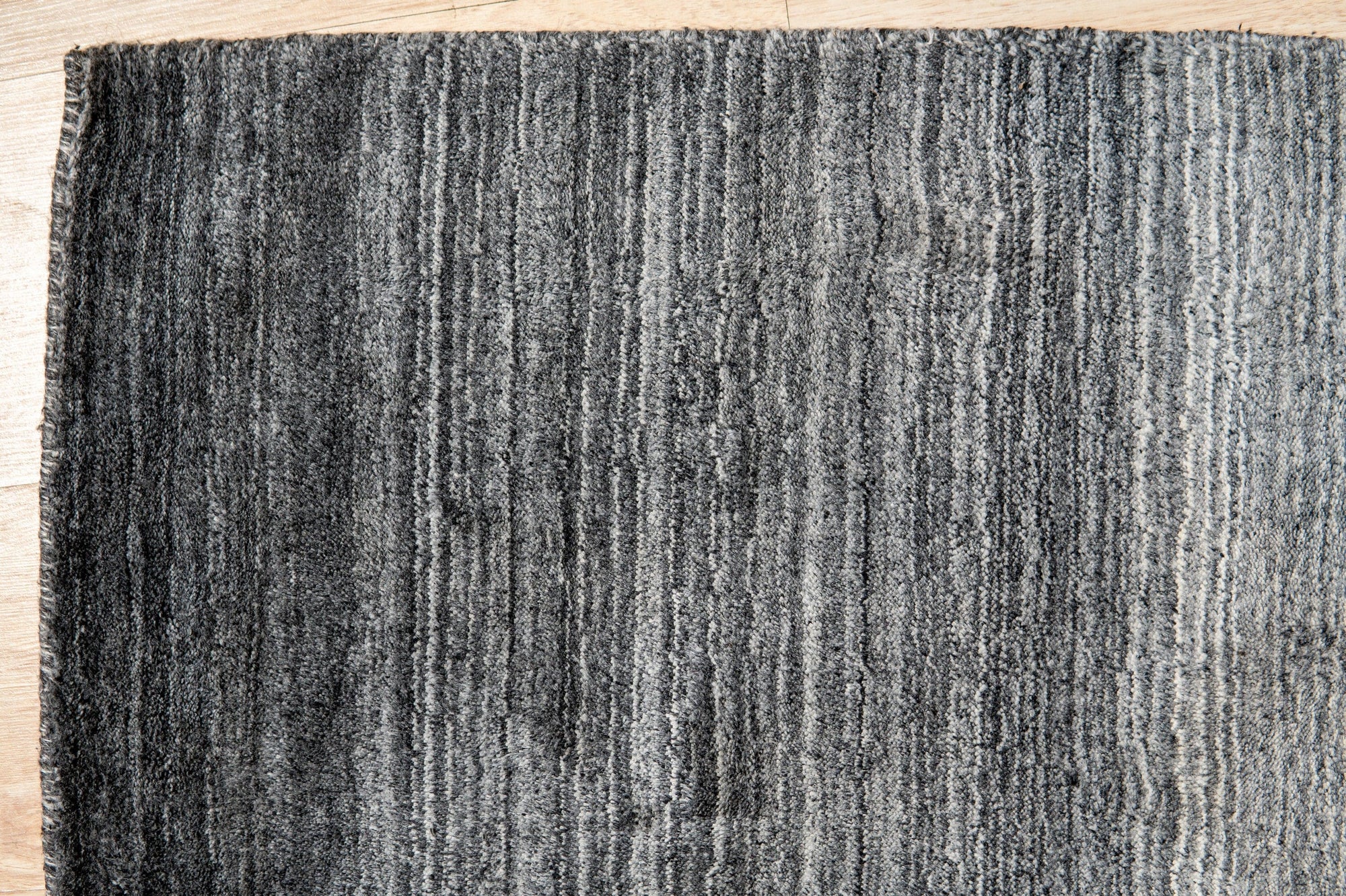 Penelope Nina Charcoal Handmade Wool Rug, showcasing intricate, textured patterns in varying shades of charcoal gray, filling a well-lit space with subtle depth and warmth.