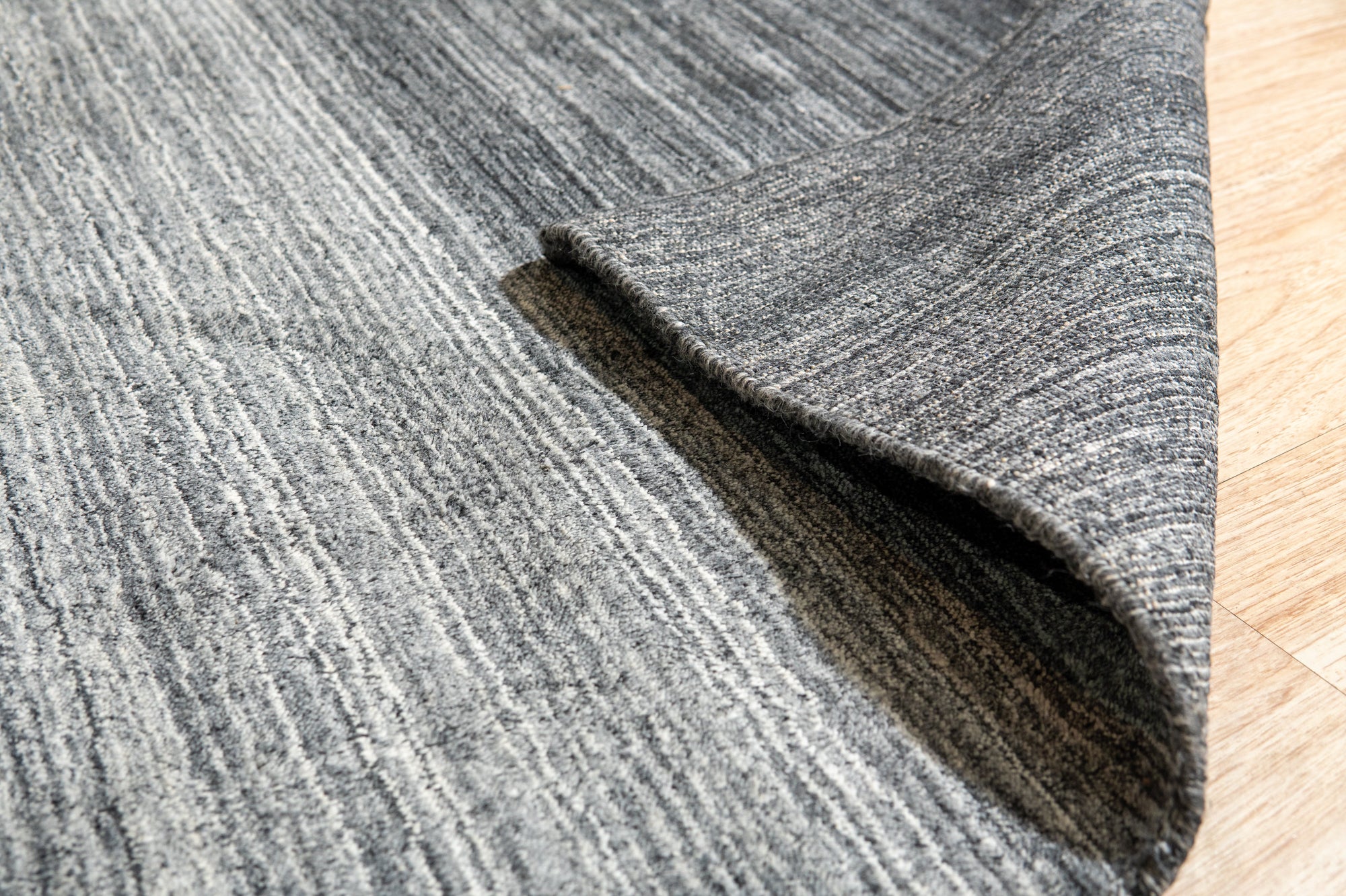Penelope Nina Charcoal Handmade Wool Rug, showcasing subtle texture and varying shades of charcoal grey wool in a modern living room setting.