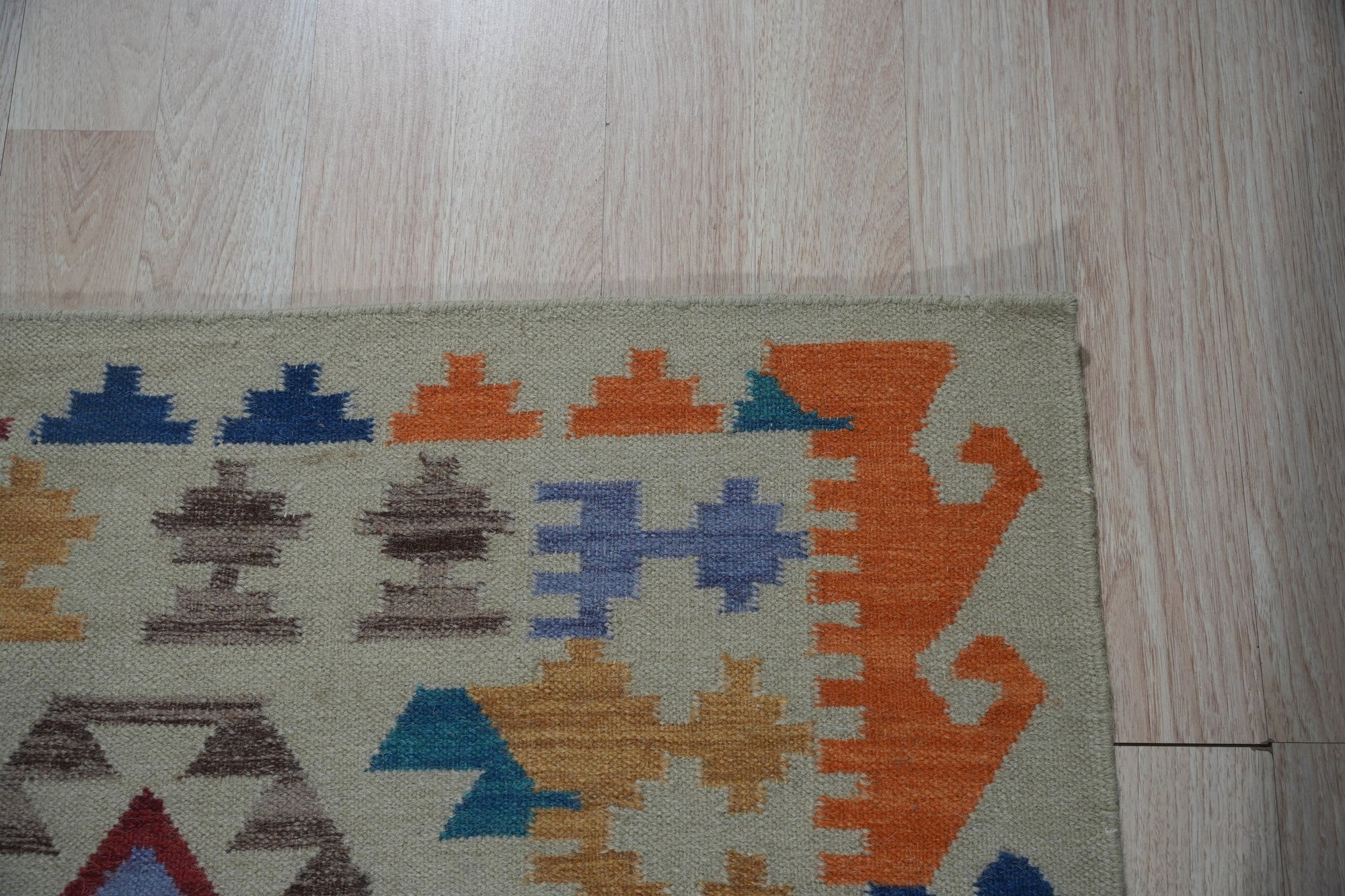 Nina Cassandra Multicolor Flatweave Wool Rug displayed on a light hardwood floor, its vibrant geometric patterns in shades of teal, orange, cream, and burgundy adding a modern touch to the space.