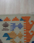 Nina Cassandra Multicolor Flatweave Wool Rug displayed on a light hardwood floor, its vibrant geometric patterns in shades of teal, orange, cream, and burgundy adding a modern touch to the space.