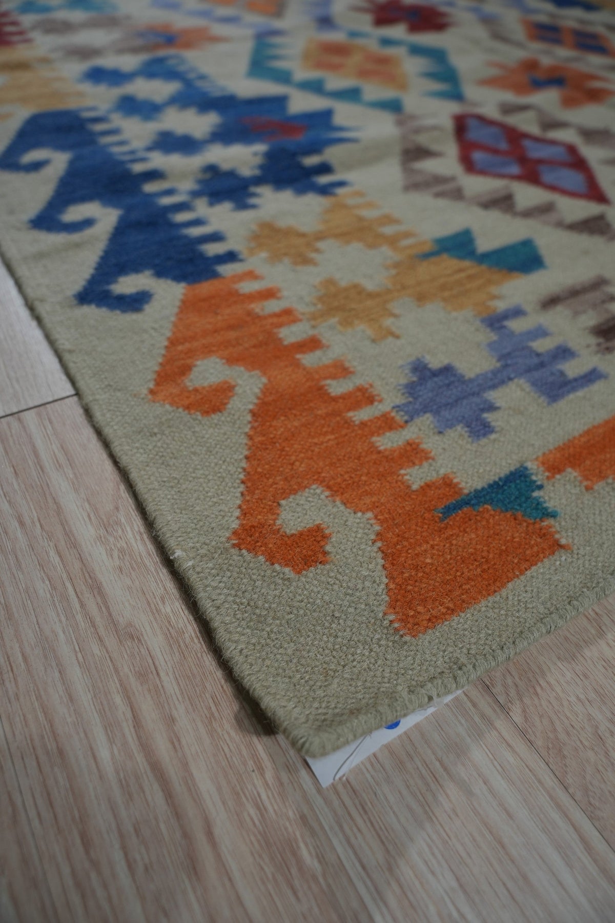 Nina Cassandra Multicolor Flatweave Wool Rug, displayed on a light wooden floor, features a vibrant geometric pattern in hues of red, blue, yellow, and beige.