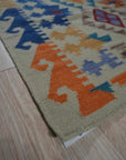 Nina Cassandra Multicolor Flatweave Wool Rug, displayed on a light wooden floor, features a vibrant geometric pattern in hues of red, blue, yellow, and beige.