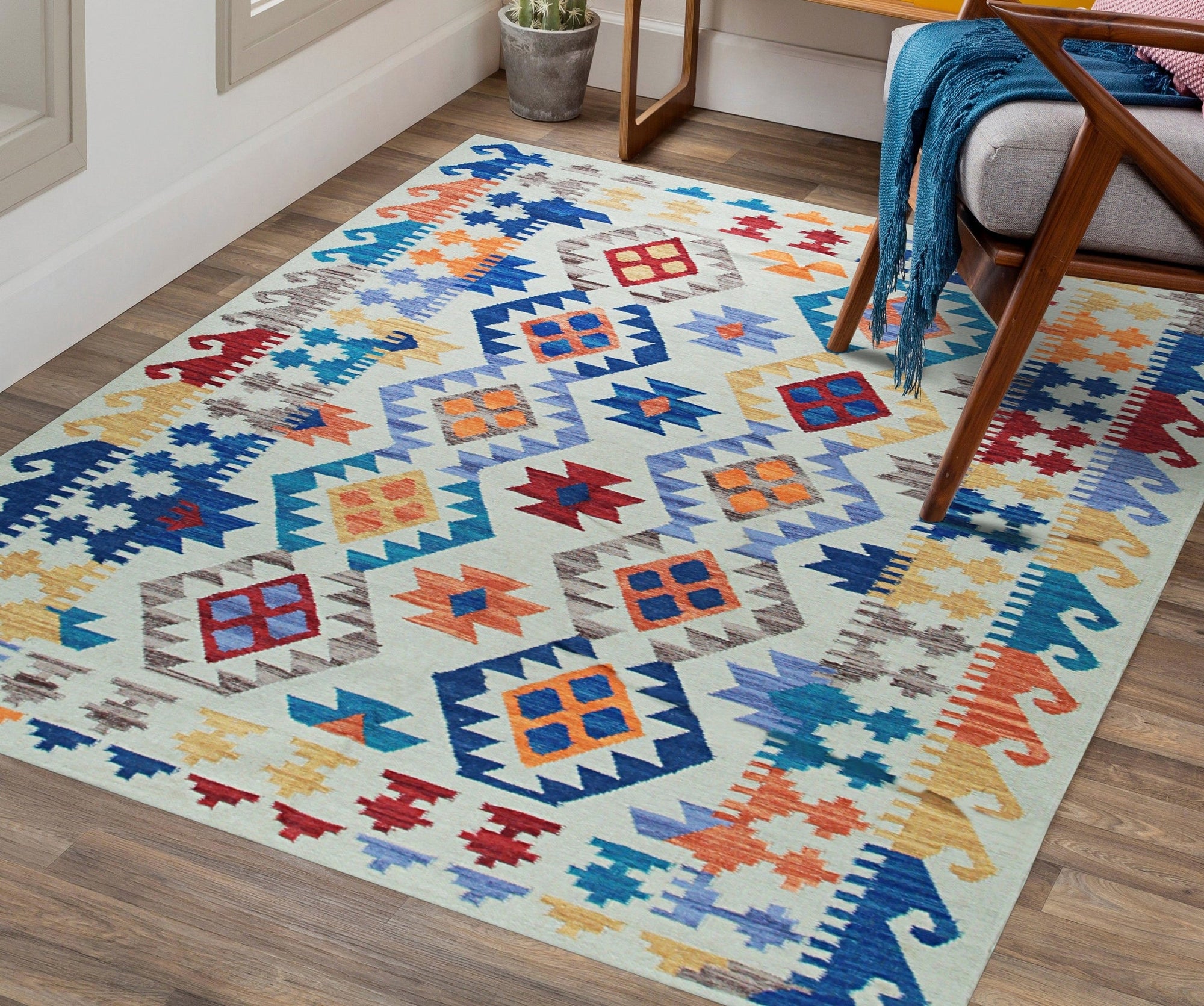 Nina Cassandra Multicolor Flatweave Wool Rug, vibrant geometric patterns in blues, oranges, and yellows dance across this wool rug, seen in a modern living room setting with a mid-century style chair.