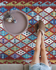 Amara Kilim Multicolor Flatweave Wool Rug, a vibrant patchwork of geometric patterns in warm and cool tones, lies flat on a light-colored hardwood floor, adding a global-inspired touch to a modern space.