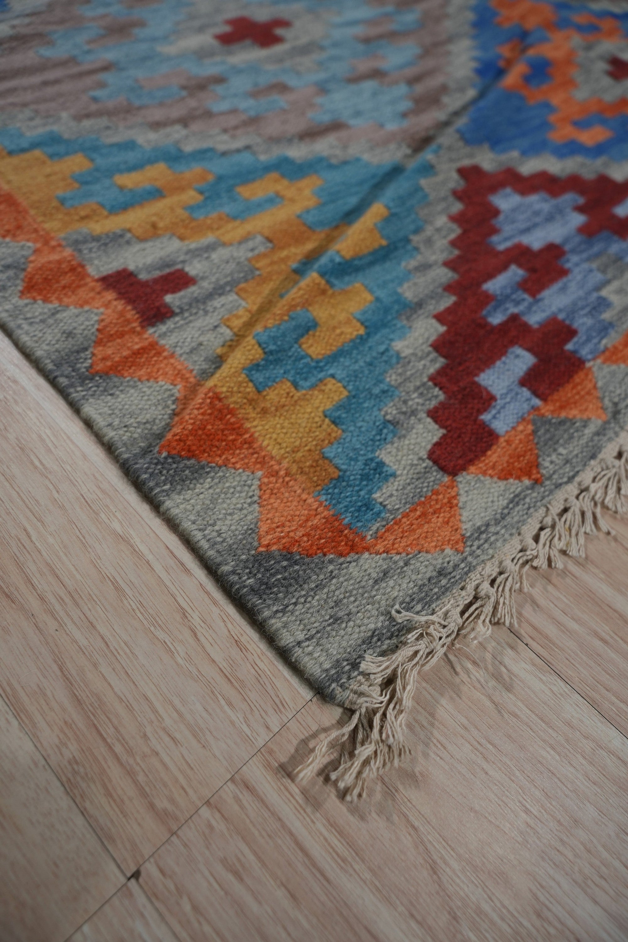 Iris Sophisticated Multicolor Flatweave Wool Rug, showcasing a vibrant geometric pattern in shades of blue, orange, red, and cream, laid flat with a subtle sheen on its wool fibers.