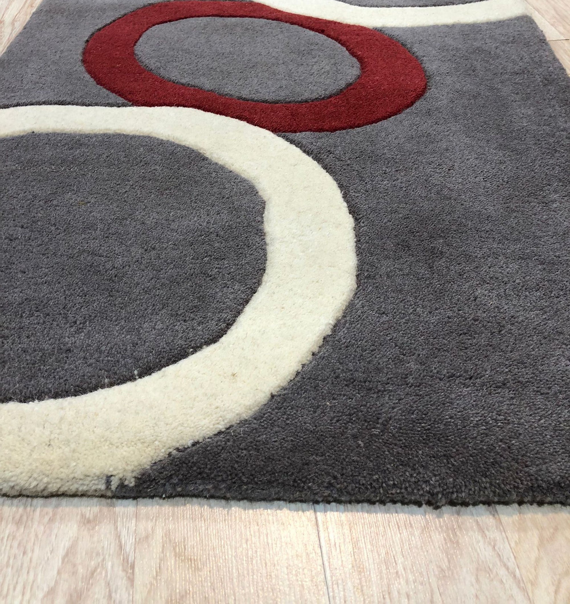 Celia Clara Gray Hand Tufted Wool Rug, showcasing a subtle geometric pattern in varying shades of gray, lies on a light hardwood floor, suggesting warmth and understated elegance.
