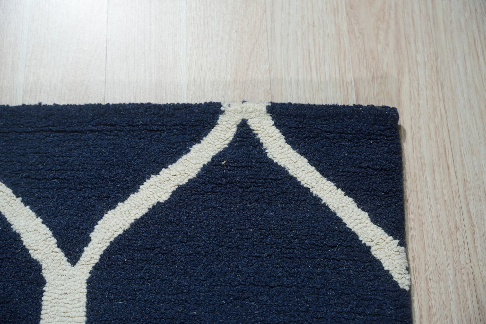 Jasmine Artisan Blue Hand Tufted Wool Rug in a bright, airy living room. Light filters across the rug's textured surface, showcasing its hand-tufted wool construction and vibrant blue hues. A comfortable seating area surrounds the rug, suggesting a cozy and inviting atmosphere.