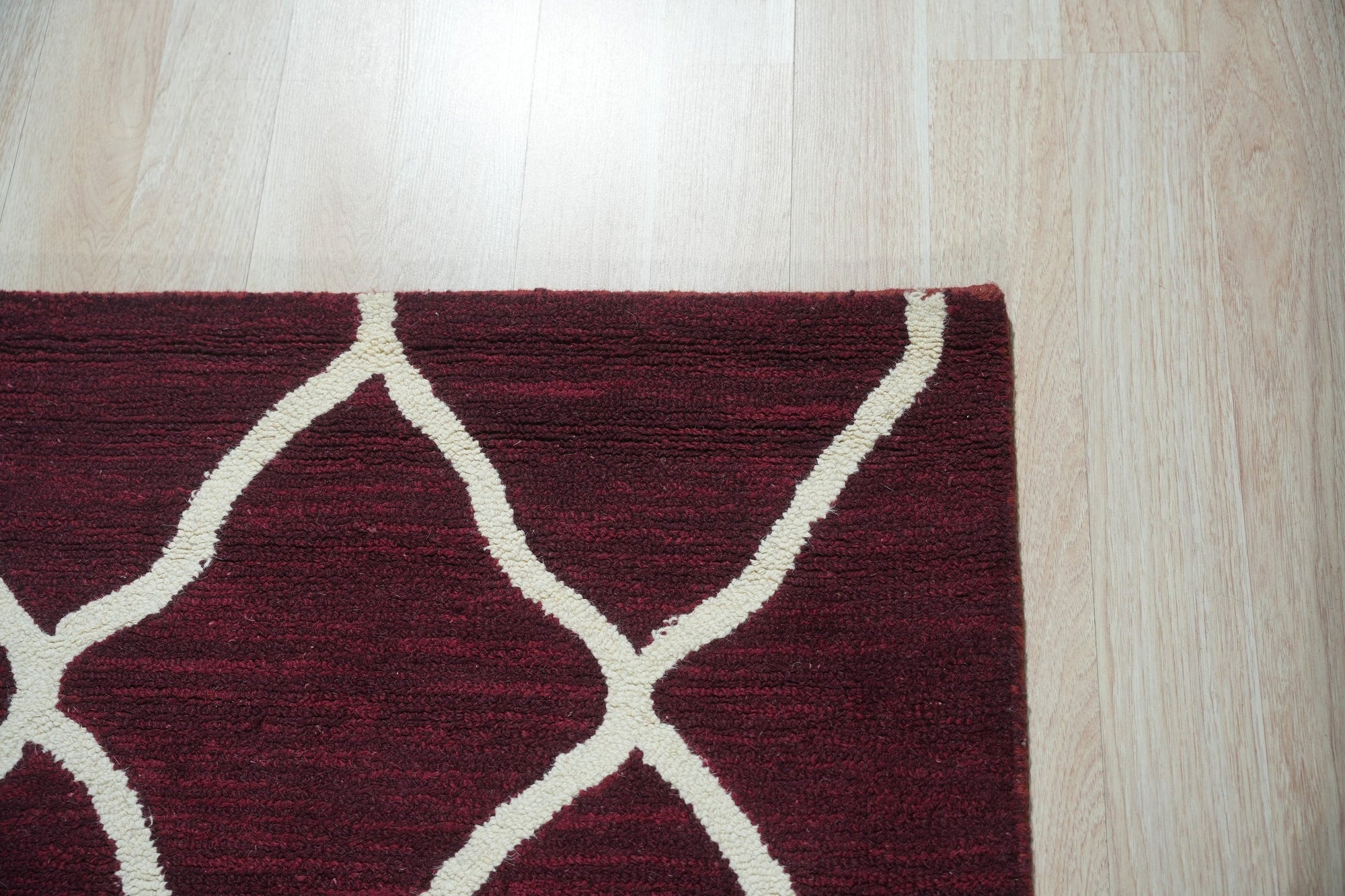 Timeless Louie Burgundy Hand Tufted Wool Rug, a rich burgundy wool rug with an ornate, traditional pattern, displayed on a light hardwood floor in a brightly lit room.