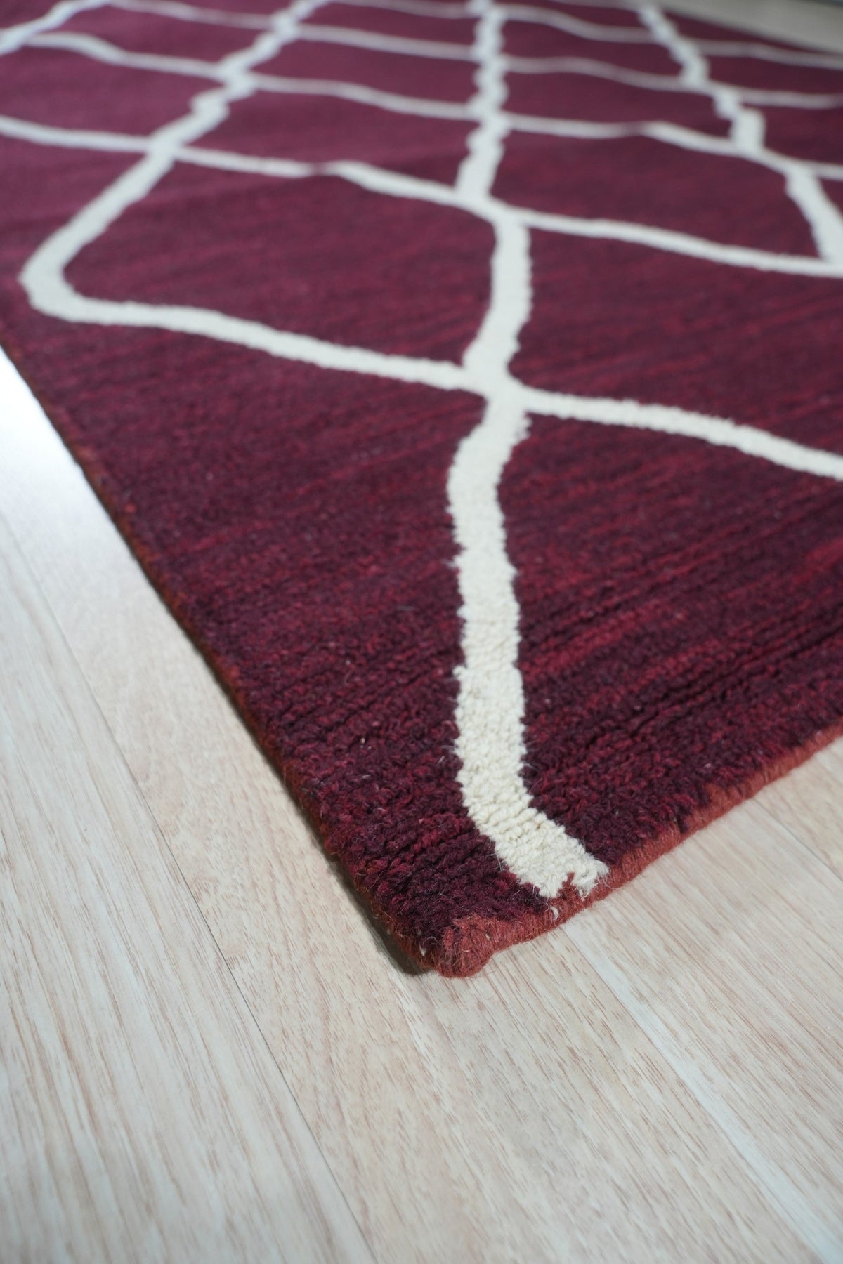 Timeless Louie Burgundy Hand Tufted Wool Rug, richly patterned, anchors a sophisticated living space. Warm light highlights the deep burgundy hues and textured hand-tufted wool, complemented by neutral furniture and hardwood floors.