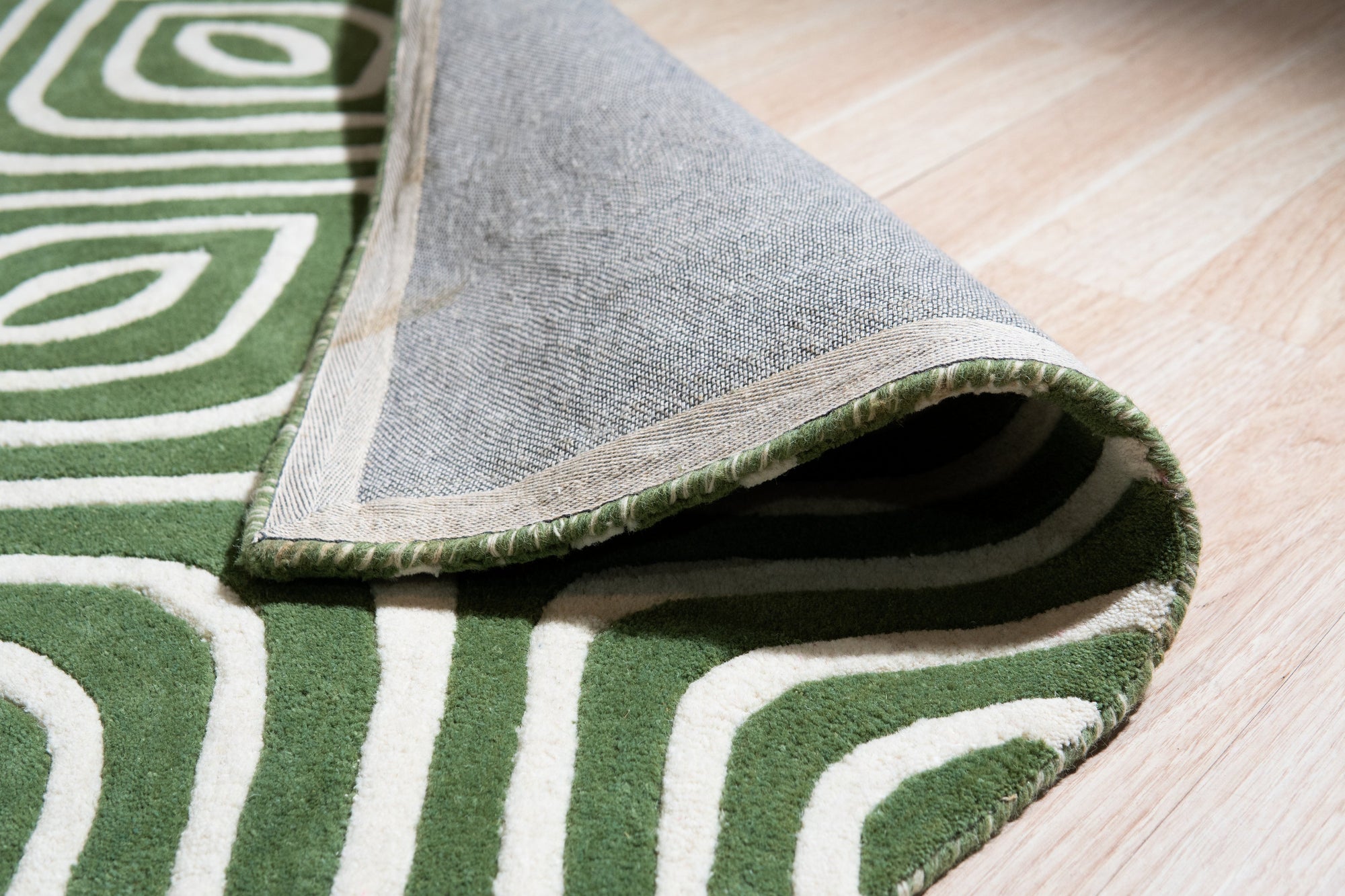 Radiant Amara Green Hand Tufted Wool Rug, showcasing its lush green tones and hand-tufted texture, rests gracefully on a light-colored wood floor, creating a vibrant contrast in a modern living space.