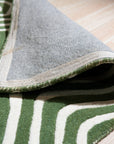 Radiant Amara Green Hand Tufted Wool Rug, showcasing its lush green tones and hand-tufted texture, rests gracefully on a light-colored wood floor, creating a vibrant contrast in a modern living space.