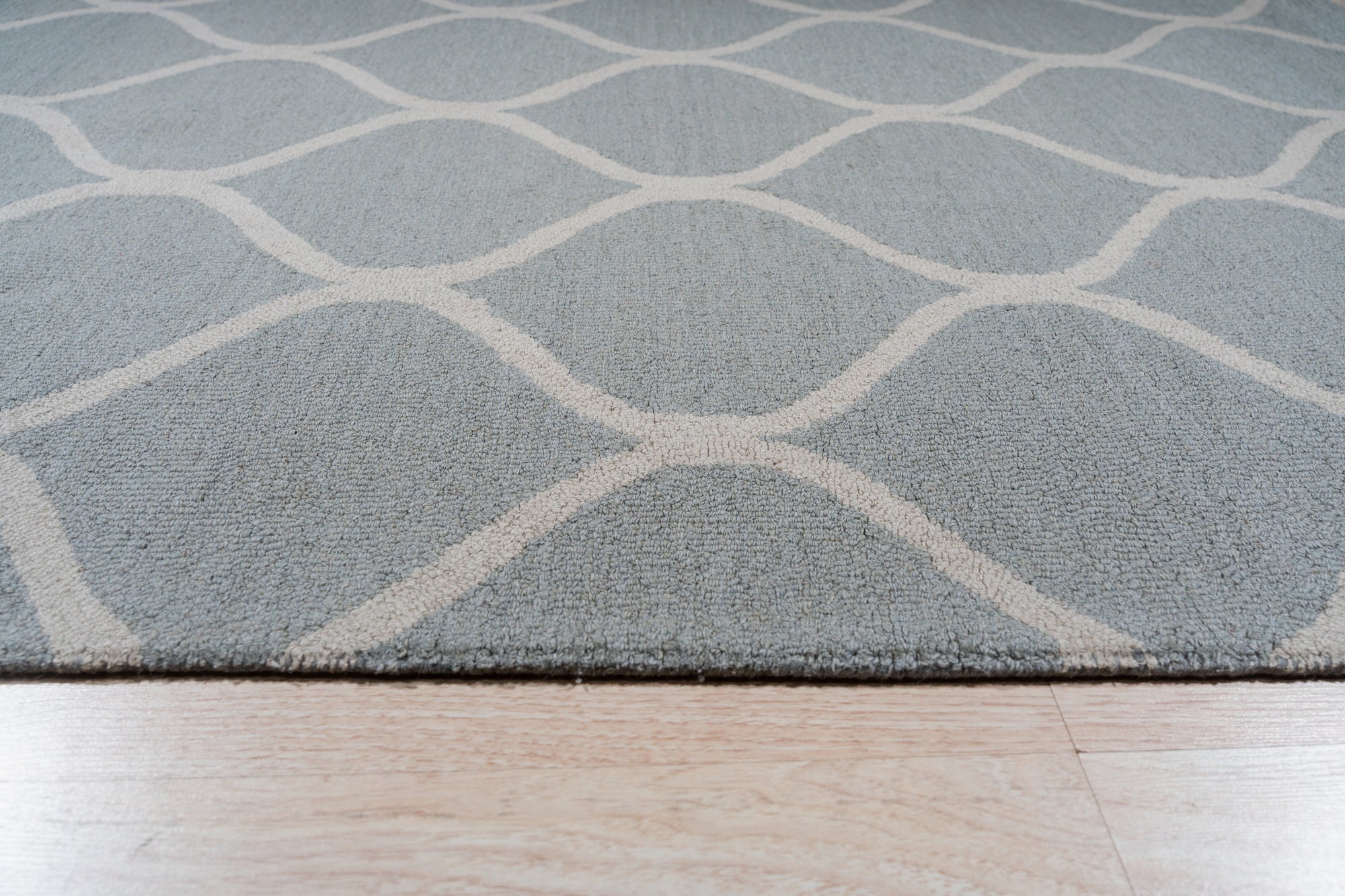 Handcrafted Laine Light Green Hand Tufted Wool Rug, a light green wool rug with a subtle geometric pattern, grounding a modern living room with warm lighting and a glimpse of a dining area beyond.
