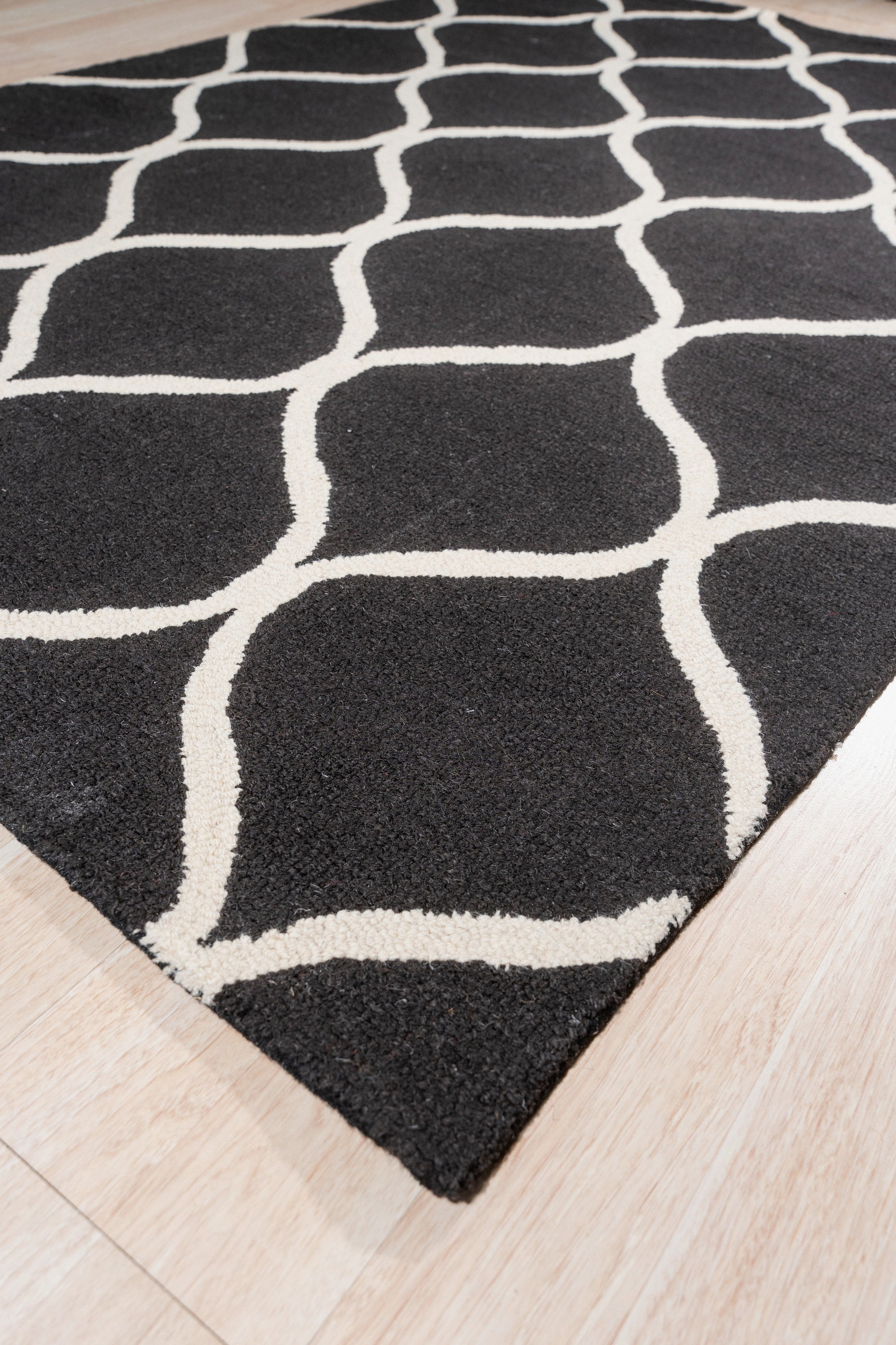 Sloane Willow Navy Hand Tufted Wool Rug, displaying a muted botanical pattern in shades of navy, cream, and gray, laid on a dark hardwood floor beneath a light-colored sofa with patterned throw pillows, creating a cozy and inviting living space.