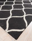 Sloane Willow Navy Hand Tufted Wool Rug, displaying a muted botanical pattern in shades of navy, cream, and gray, laid on a dark hardwood floor beneath a light-colored sofa with patterned throw pillows, creating a cozy and inviting living space.