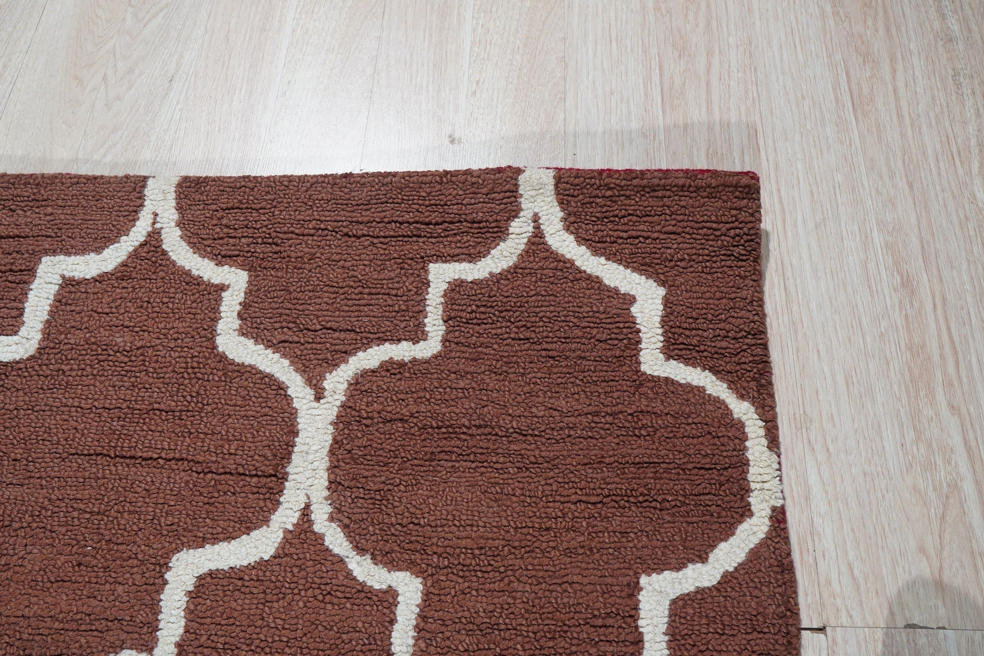 Trendy Moroccan Rust Hand Tufted Wool Rug, a vibrant geometric design in earthy rust tones, layered atop a light hardwood floor in a bright, modern living room.