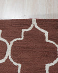 Trendy Moroccan Rust Hand Tufted Wool Rug, a vibrant geometric design in earthy rust tones, layered atop a light hardwood floor in a bright, modern living room.