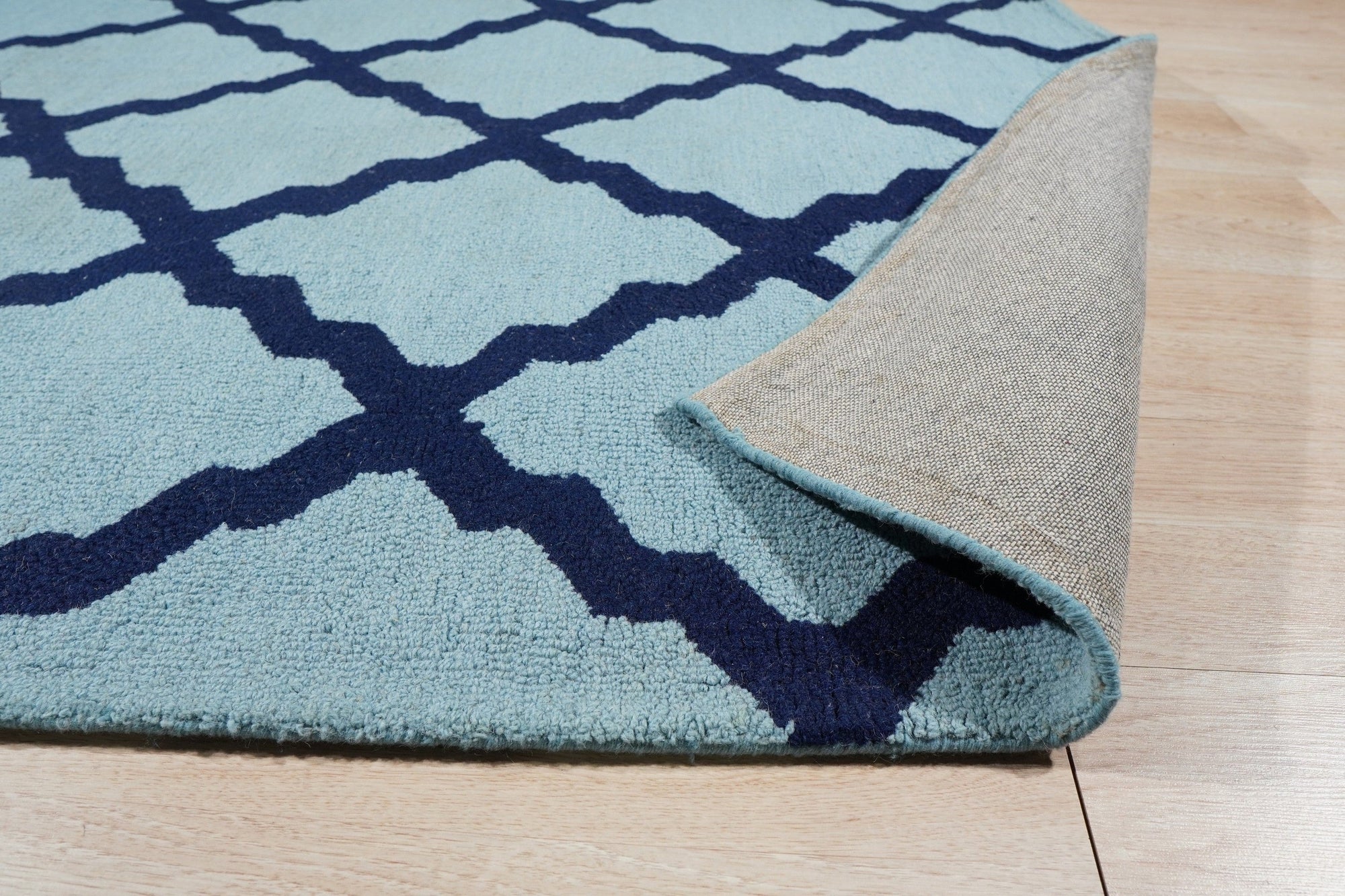 Bianca Trellis Sea Blue Hand Tufted Wool Rug, featuring a delicate trellis pattern in varying shades of sea blue, graces a softly lit room, adding texture and subtle elegance to the space.