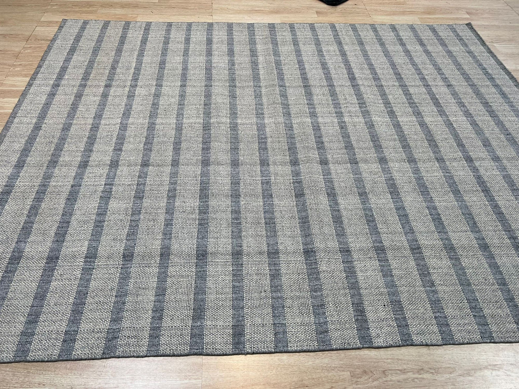 Luxurious Timeless Gray Handmade Wool Rug, soft gray wool pile inviting touch, rests on dark wood flooring, showcasing subtle pattern variations under natural light spilling from a nearby window.