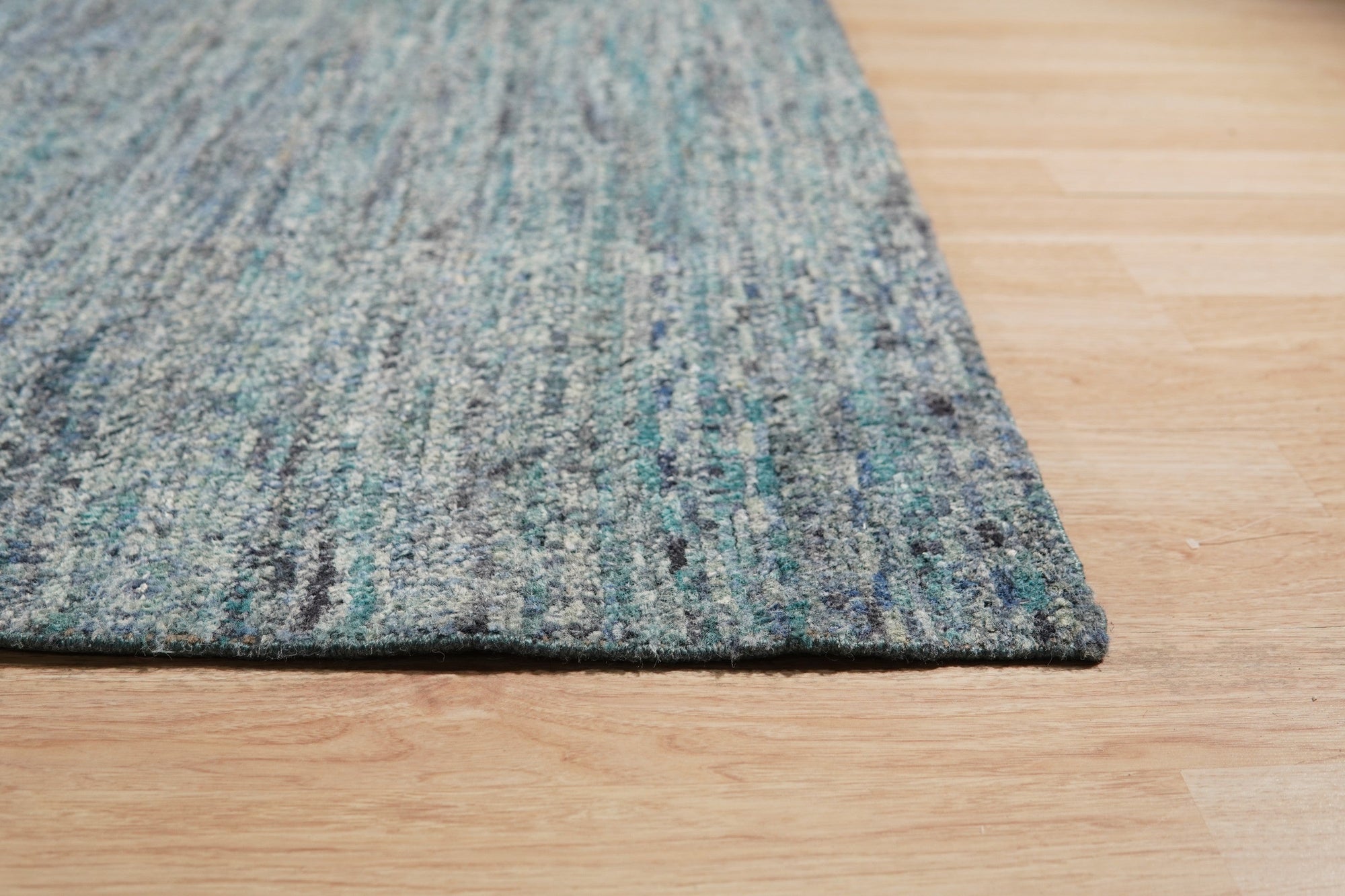 Jade Elegant Blue Hand Knotted Silk Rug, showcasing intricate patterns and shimmering silk fibers, lies flat on a light surface, its rich blue hues and delicate knotting details clearly visible.