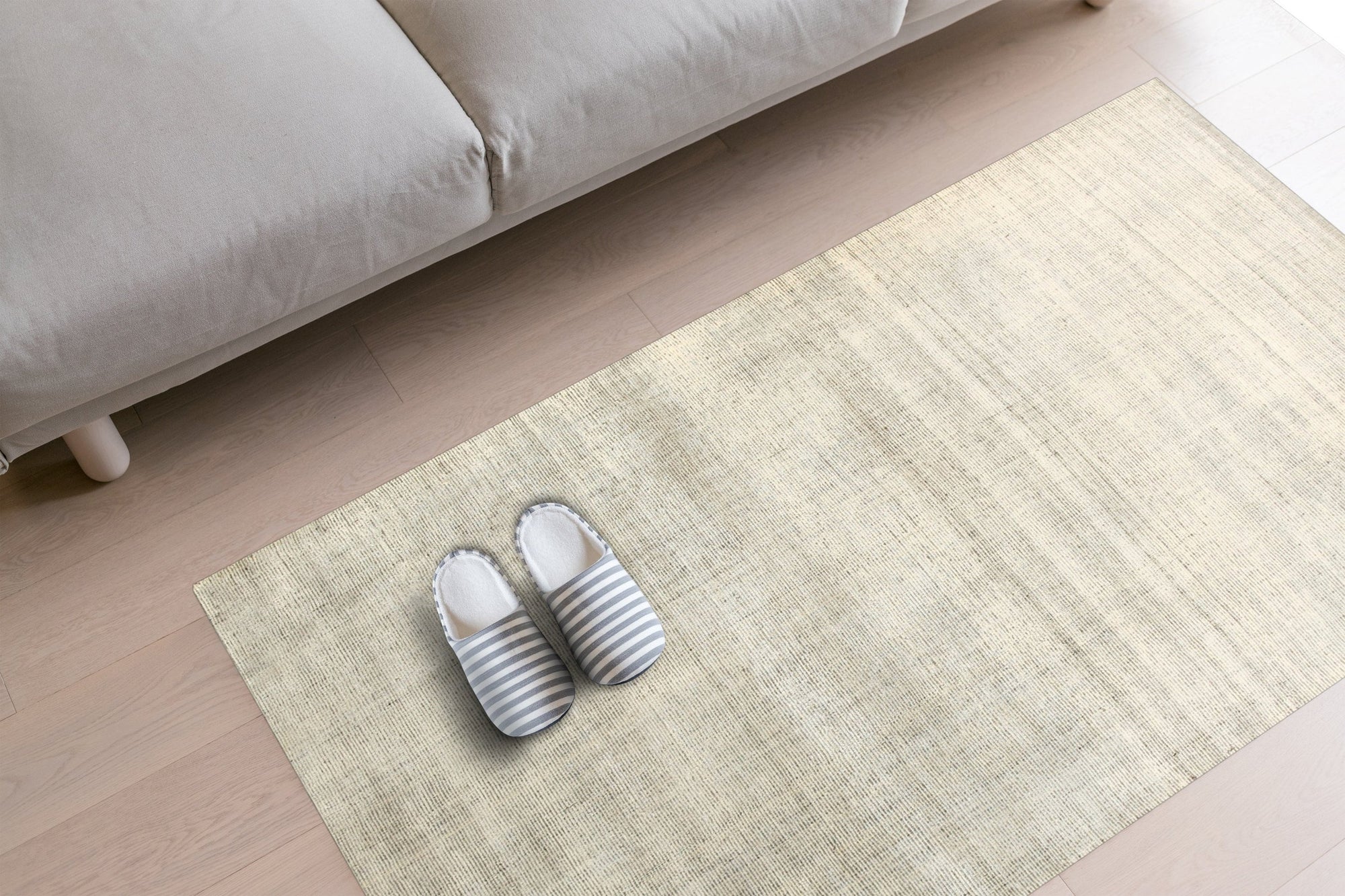 Talia Artisan Gray Handmade Rug, woven with subtle textures, rests on a light wooden floor beside a modern gray sofa, its gray hues complementing the minimalist setting.