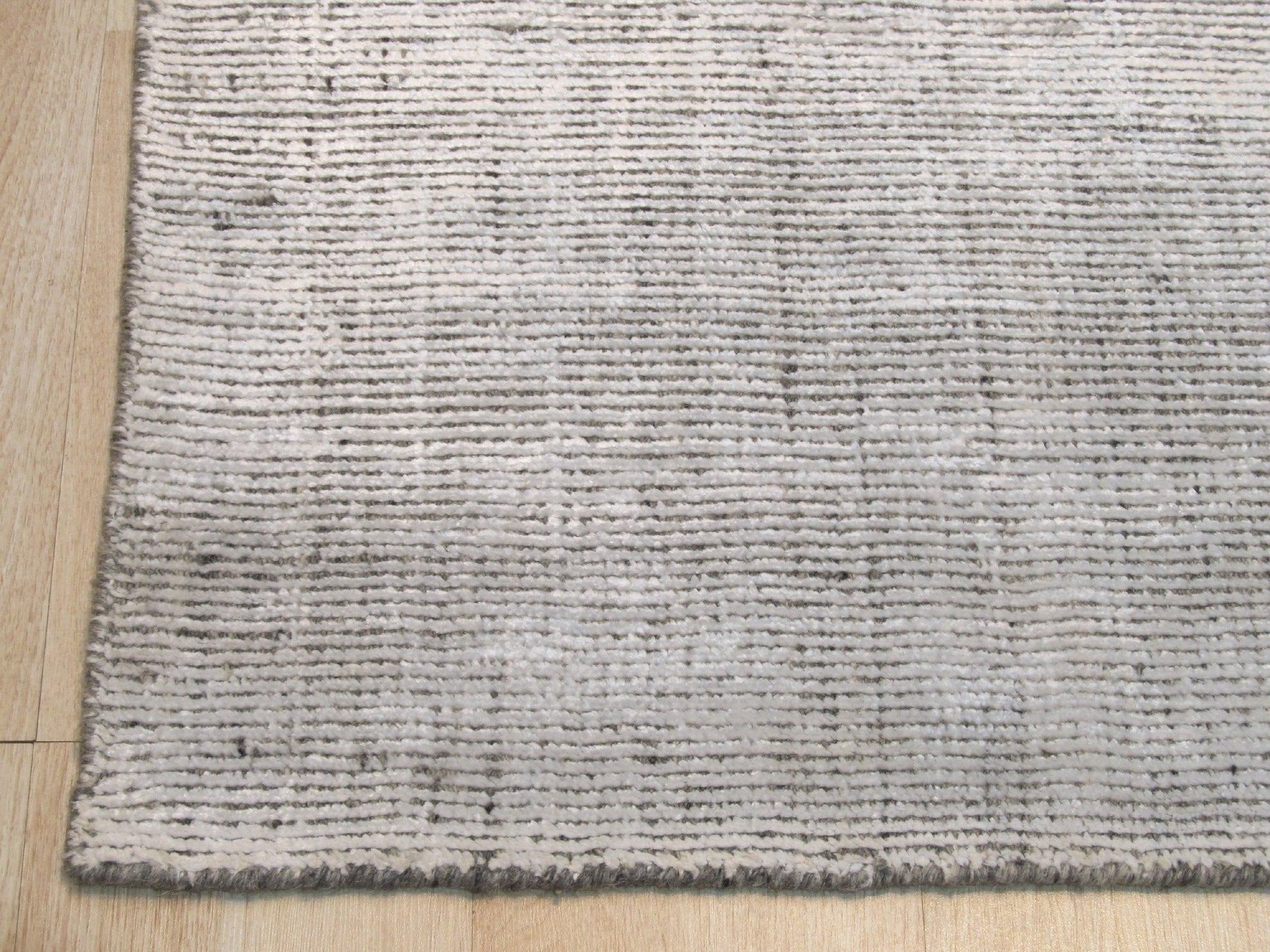 Talia Artisan Gray Handmade Rug displayed in a bright living room setting, its neutral gray tones complementing a modern sofa and wooden coffee table.