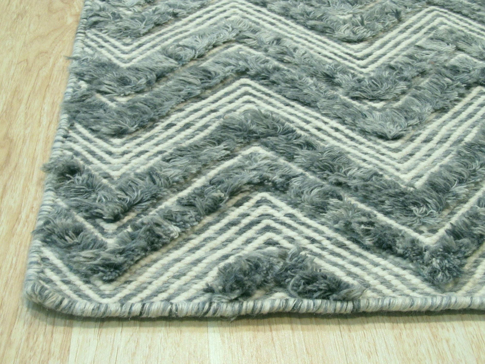Charming Trara Green Handmade Wool Rug, lush green wool rug with subtle variations in color, resting on a dark hardwood floor with a cream-colored wall in the background, showcasing its handcrafted texture and inviting warmth.