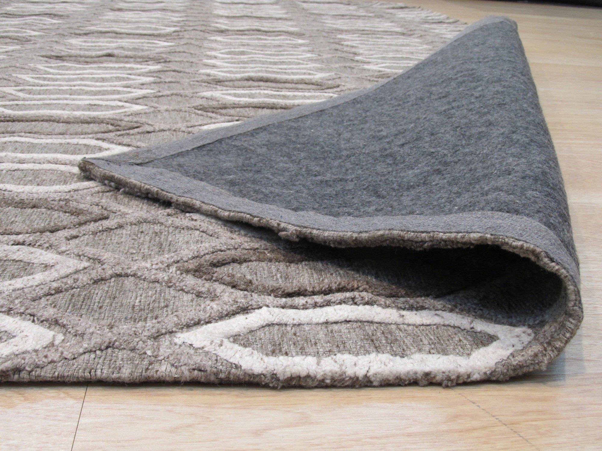 Lila Trellis Gray Nan Rug, a gray rug featuring a subtle trellis pattern, laid on a light wood floor. Natural light illuminates the soft, nan-material texture.
