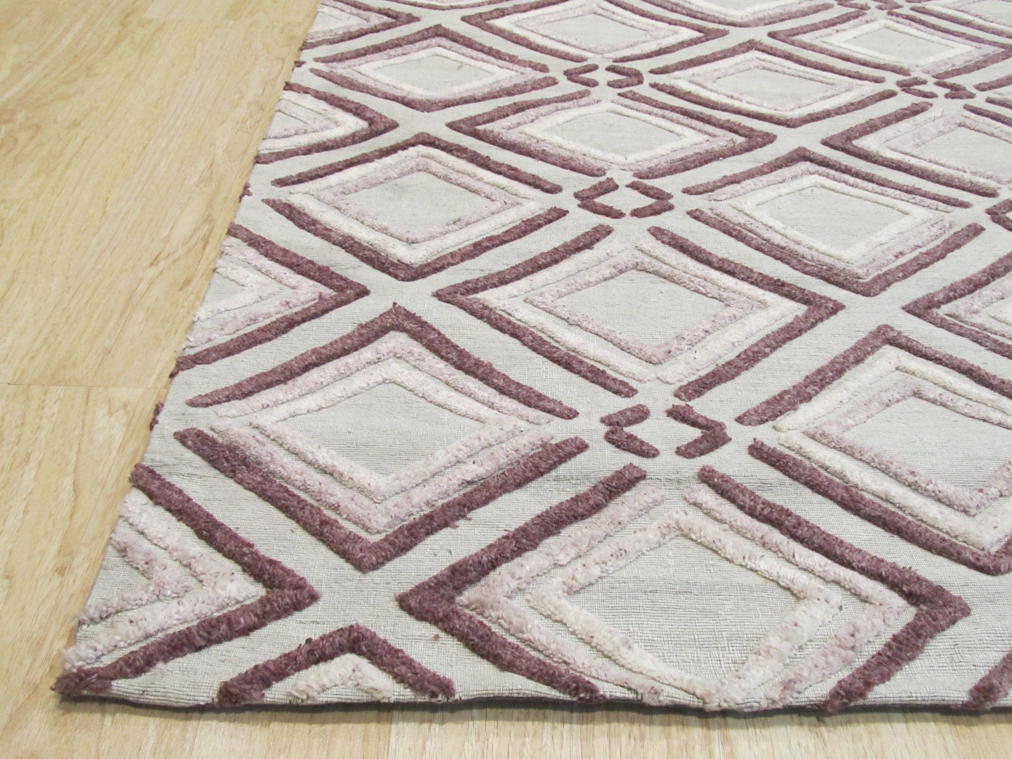 Isla Diamond Purple Hand Knotted Wool Rug, plush wool fibers displaying an intricate diamond pattern in shades of purple and cream, partially visible in a styled interior setting.