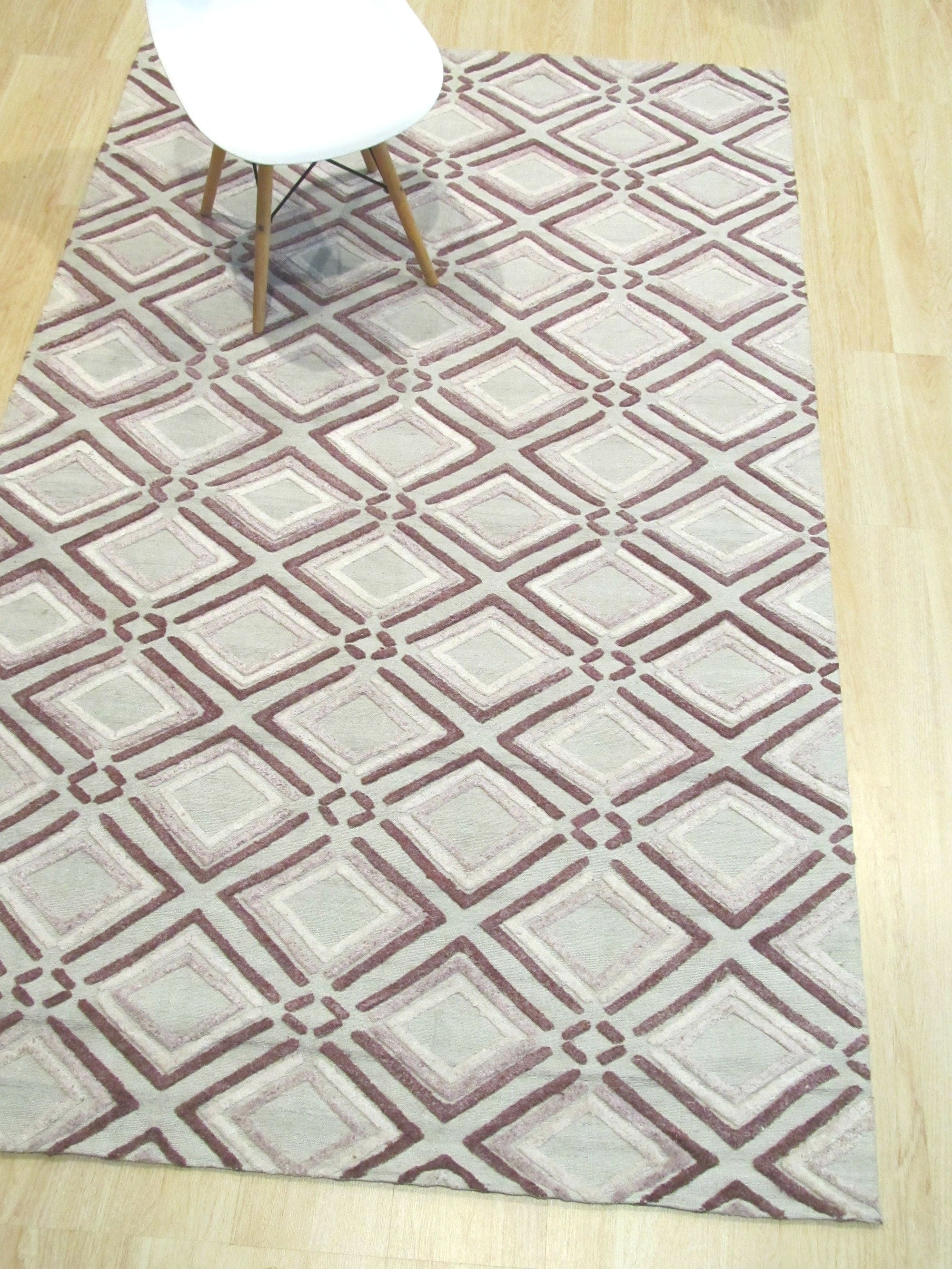 Isla Diamond Purple Hand Knotted Wool Rug, a luxurious purple hand-knotted wool rug with a diamond pattern, lies softly on a light wooden floor, adding a touch of elegant warmth to a bright, airy space.