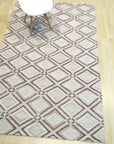 Isla Diamond Purple Hand Knotted Wool Rug, a luxurious purple hand-knotted wool rug with a diamond pattern, lies softly on a light wooden floor, adding a touch of elegant warmth to a bright, airy space.