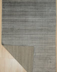 Refined Majestic Silver Handmade Wool & Viscose Rug, shimmering with subtle silver hues, lays gracefully on a hardwood floor. The luxurious pile invites touch, highlighting the intricate handmade construction in a comfortable living room setting.