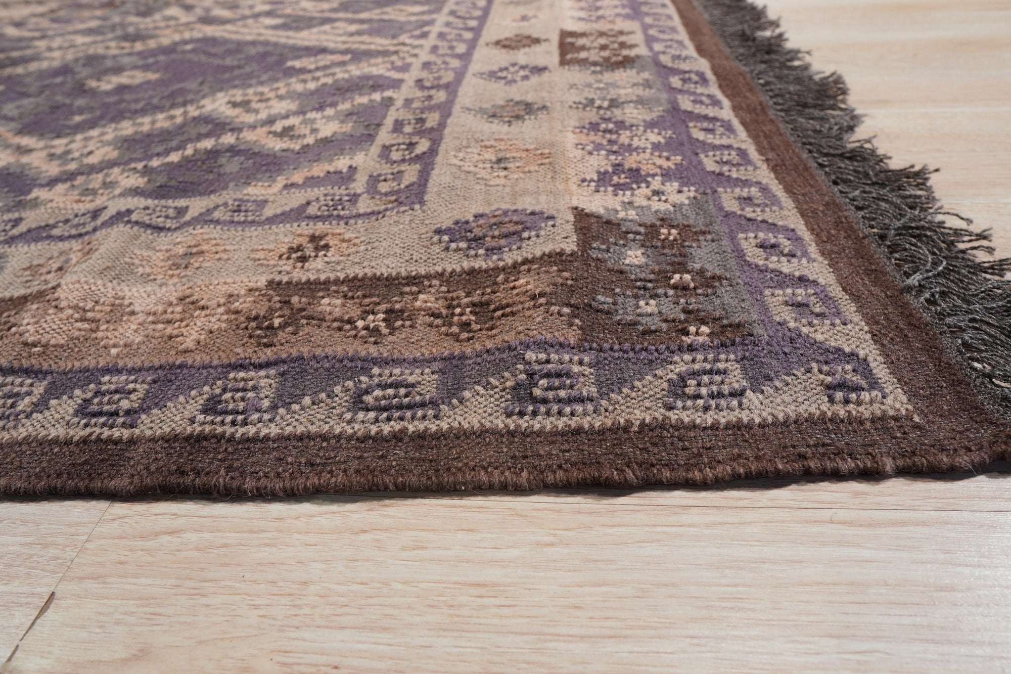 Brenda Jasmine Brown Flatweave Wool Rug, showcasing a warm, inviting design with intricate geometric patterns in varying shades of brown and beige, laid out in a bright living room setting.