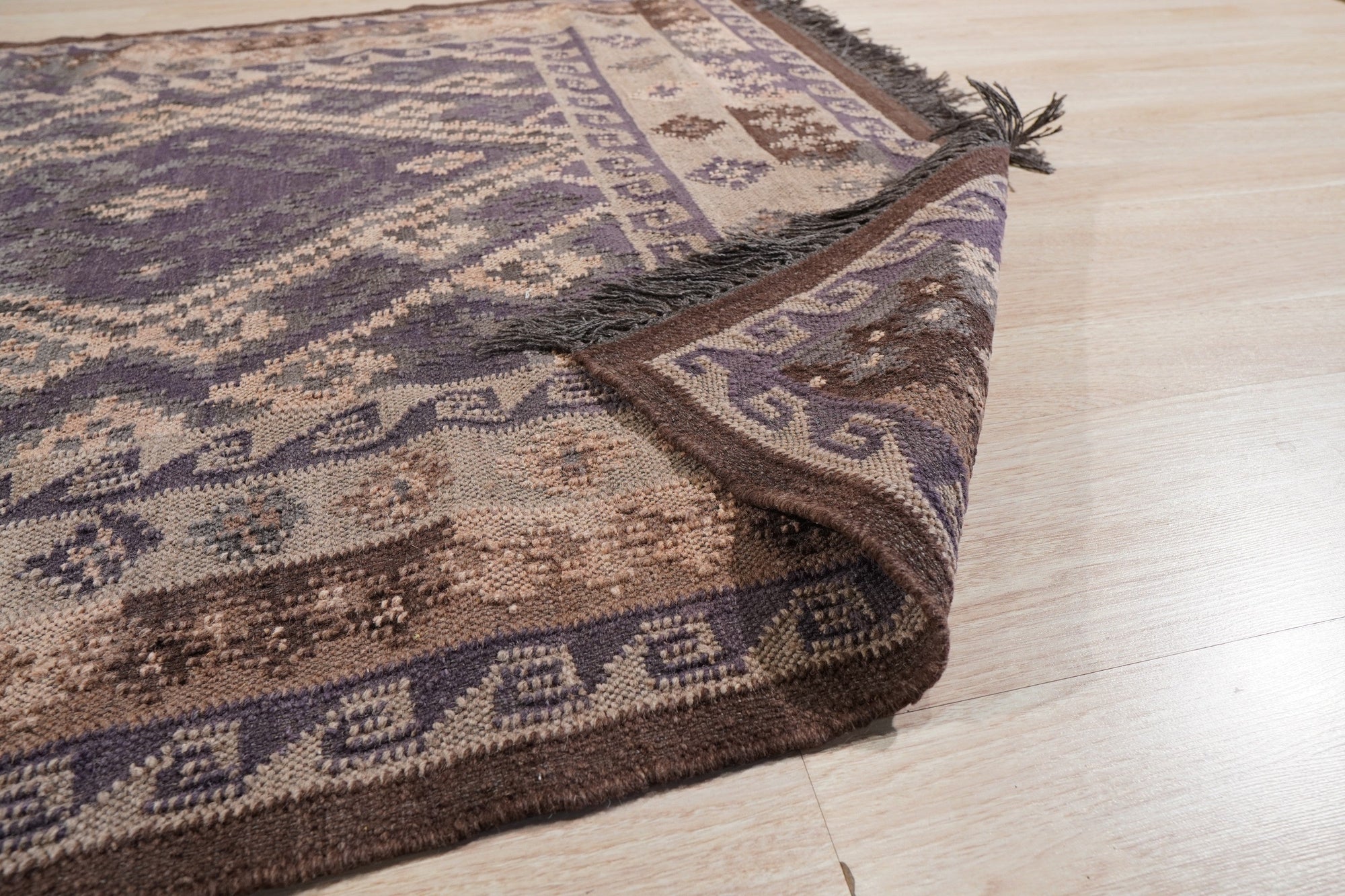 Brenda Jasmine Brown Flatweave Wool Rug, woven from wool with a flatweave construction, features brown tones and intricate patterns, complementing a naturally lit room with neutral furniture.