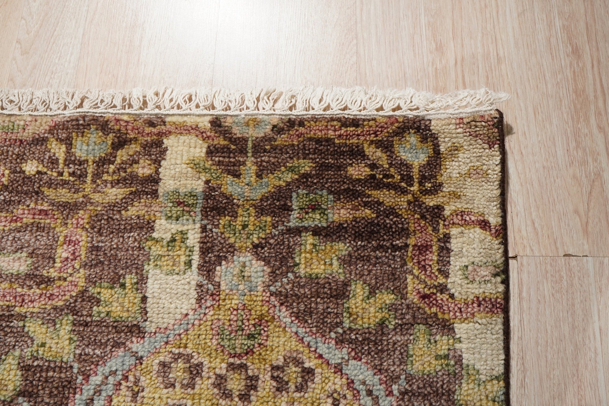 Iris Sophisticated Brown Hand Knotted Wool Rug, seen in a bright, naturally lit living room. Neutral walls and warm wood accents complement rug's sophisticated, earthy brown tones and intricate hand-knotted texture.