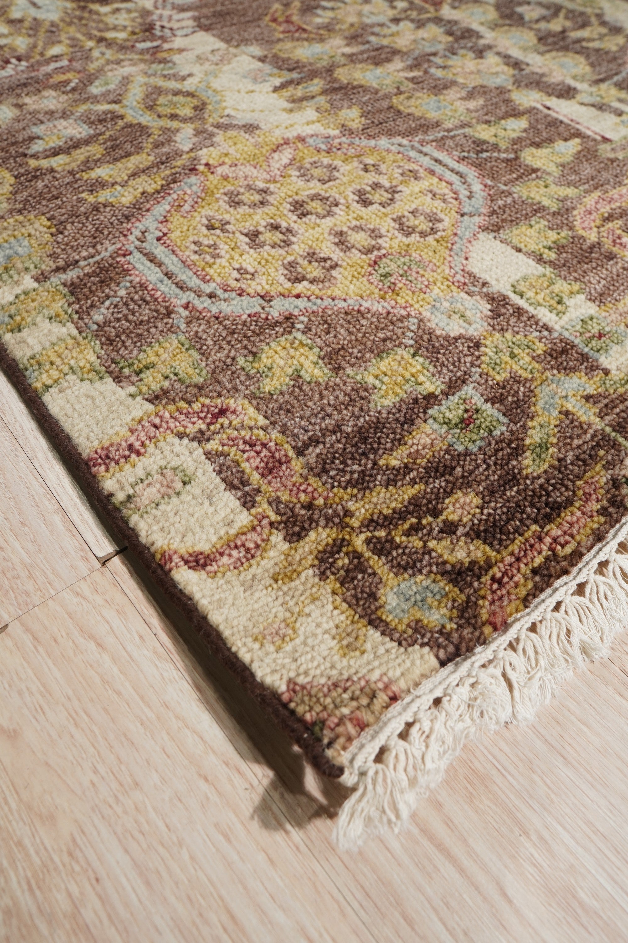 Iris Sophisticated Brown Hand Knotted Wool Rug, luxurious and warm, lays elegantly in a bright, modern living room. Warm browns and subtle patterns complement the neutral decor, highlighting the rug's intricate hand-knotted construction and plush wool texture.