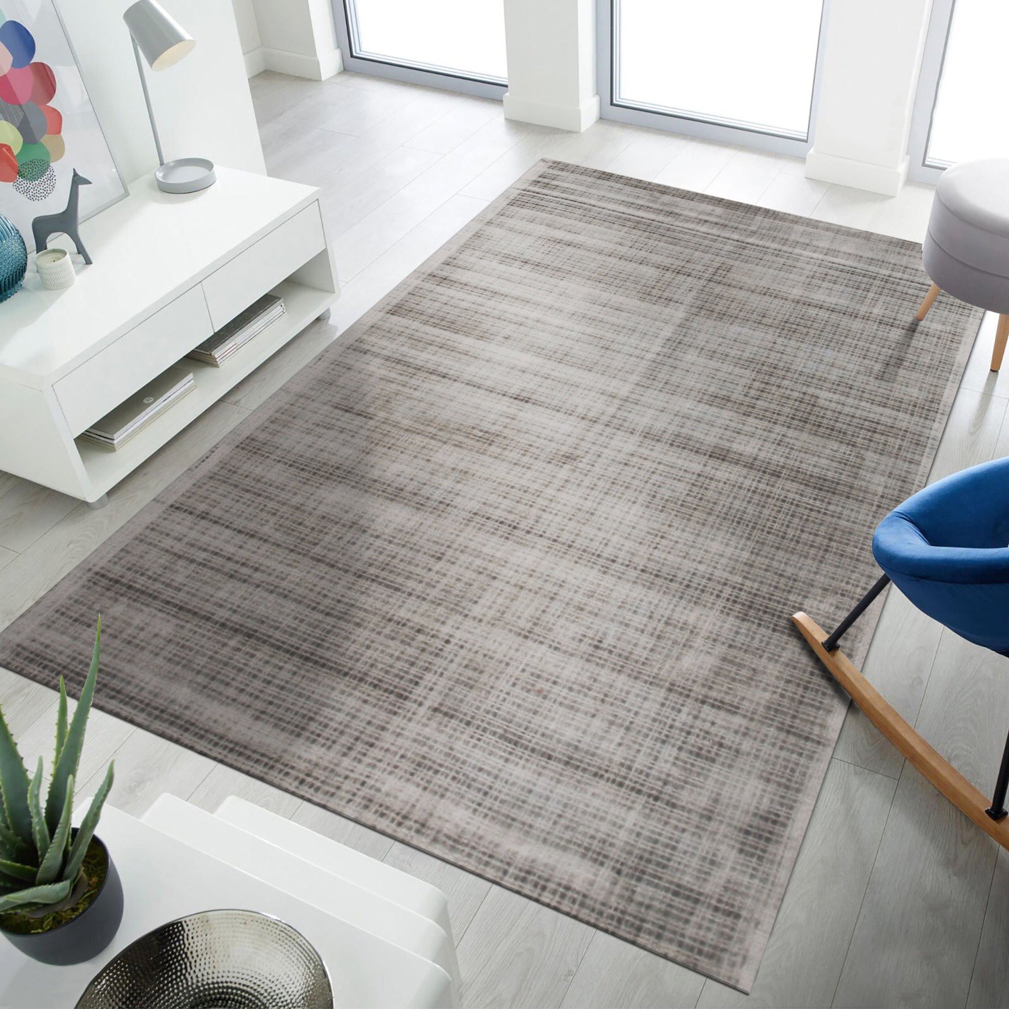 Sloane Maya Silver Handmade Rug graces a living room; neutral walls and furniture complement its shimmering silver hues and subtly textured handmade construction, adding a touch of modern elegance to the space.