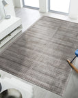 Sloane Maya Silver Handmade Rug graces a living room; neutral walls and furniture complement its shimmering silver hues and subtly textured handmade construction, adding a touch of modern elegance to the space.