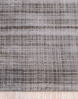 Sloane Maya Silver Handmade Rug gracing a living room, its subtle silver hues and textural weave complement a modern grey sofa and sleek wooden coffee table. Warm light illuminates the rug's intricate pattern, creating a cozy and inviting atmosphere.