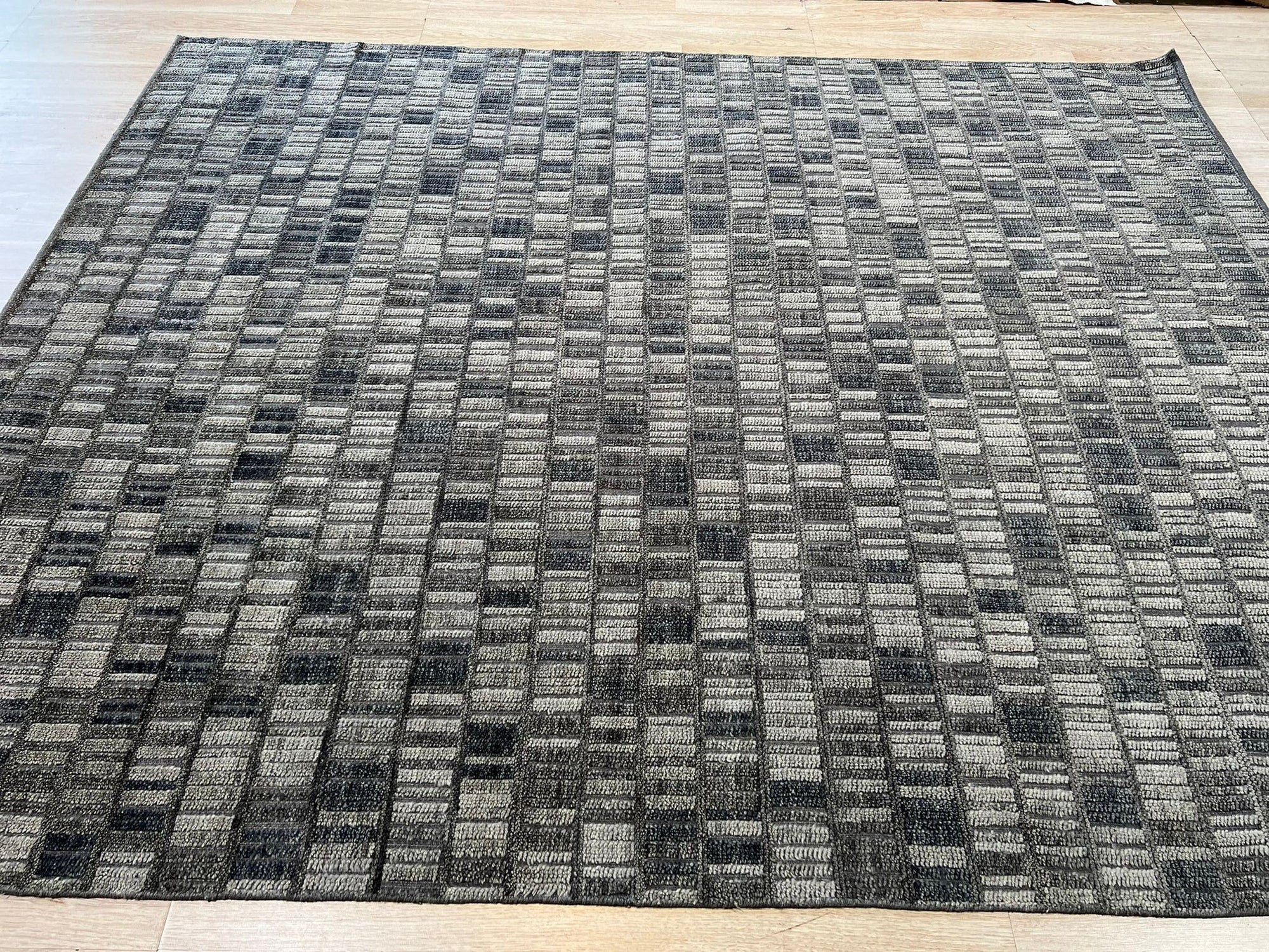 Tessa Sophisticated Gray Hand Knotted Wool Rug, grounding a light-filled living space, its subtle gray tones and hand-knotted texture adding refined warmth beneath a modern coffee table and cream-colored seating.