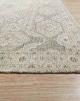 Tessa Bespoke Green Handmade Wool Rug, a deep green and textured wool rug with subtle geometric patterns, laid on light wood flooring and styled with a mid-century modern chair, hinting at a warm, inviting living space.