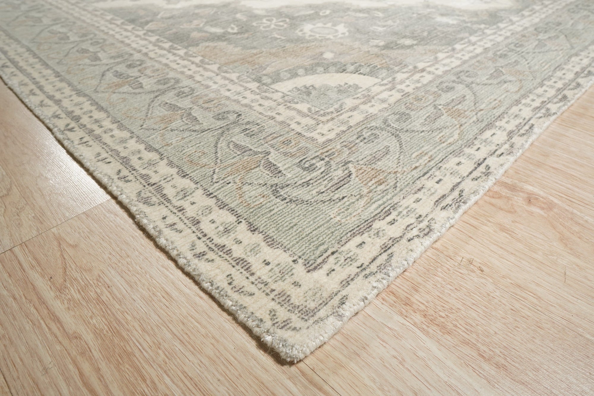 Selene Oriental Green Handmade Wool Rug, showcased in a bright living room setting. Handcrafted wool construction features an intricate oriental pattern in shades of green and cream, grounding the modern decor.