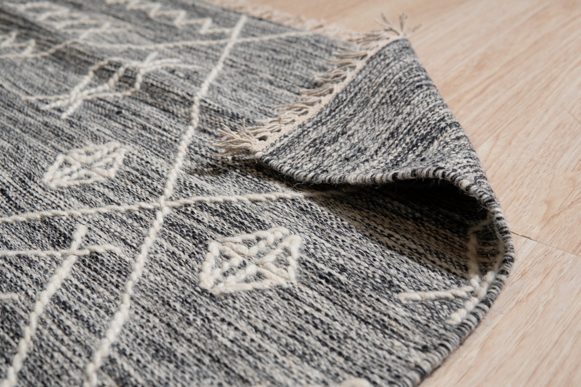 Luxurious Kilim Charcoal Handmade Wool Rug displayed as part of a stylish living room arrangement; charcoal and cream geometric patterns play across its handwoven wool surface, grounding the light-filled space with textured warmth.