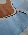 Yara Rustic Blue Hand Tufted Wool Rug, displaying deep blues and creams in a textured, hand-tufted wool construction, complements a naturally lit living space with its warm, inviting presence.
