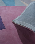 Iris Exquisite Multicolor Hand Tufted Wool Rug, vibrant jewel-toned hues swirl across this hand-tufted wool rug, adding warmth and artistic flair to a cozy living space with a textured sofa.