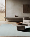Handcrafted Artisan Ivory Hand Tufted Wool Rug, a textured ivory wool rug with subtle raised patterns, partially visible under a modern glass-topped coffee table in a light-filled living room setting.